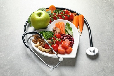 Photo of Plate of products for heart-healthy diet and stethoscope on grey table