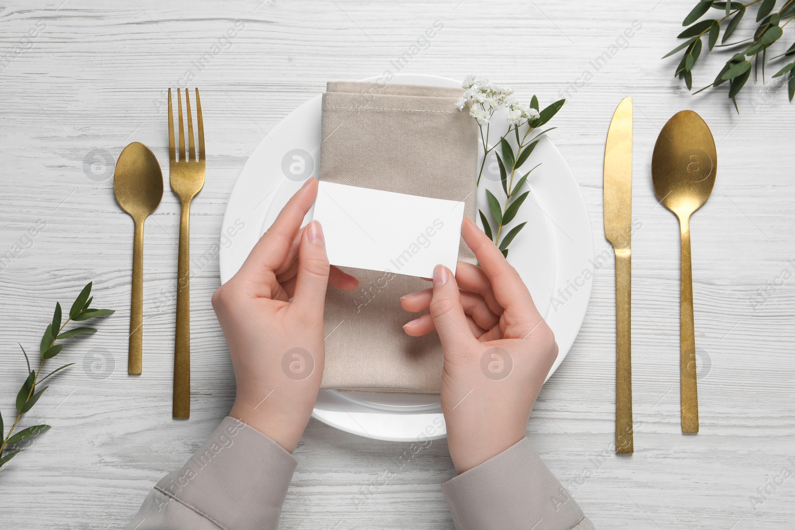 Photo of Woman holding blank card near stylish setting at white wooden table, top view. Space for text