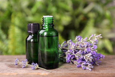Photo of Bottles with natural lavender essential oil on wooden table against blurred background