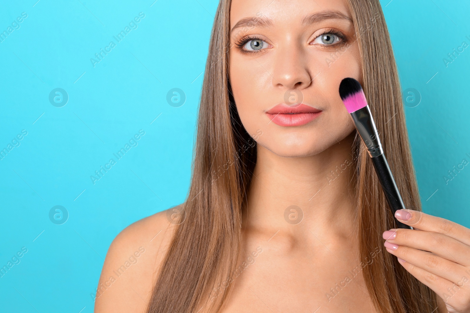 Photo of Portrait of beautiful young woman with makeup brush on color background