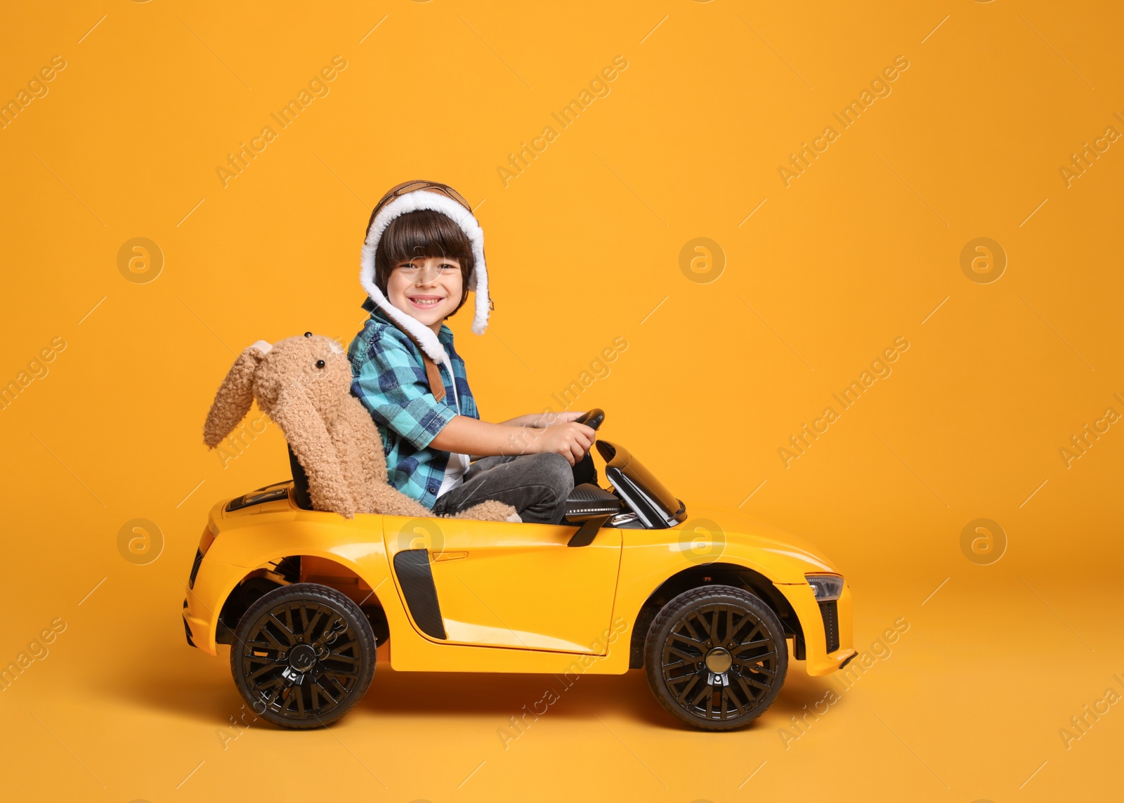 Photo of Cute little boy with toy bunny driving children's car on yellow background