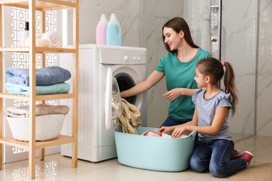 Photo of Mother and little daughter with clean laundry in bathroom