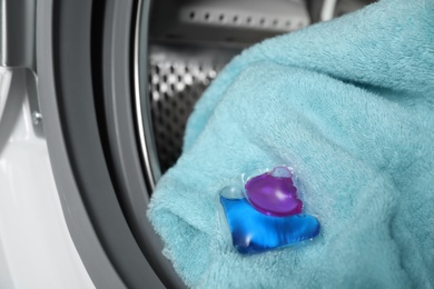 Photo of Laundry detergent capsule and towel in washing machine drum, closeup view