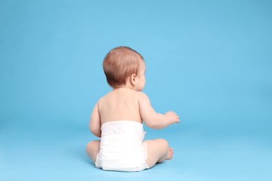 Photo of Cute little baby in diaper sitting on light blue background, back view