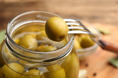 Photo of Glass jar of pickled olives and fork, closeup