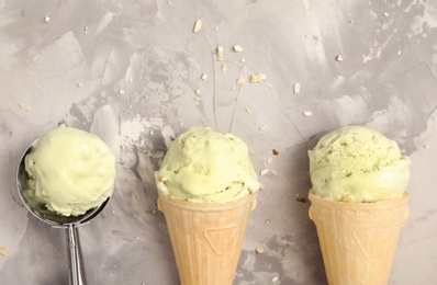 Delicious pistachio ice cream in wafer cones on light grey table, flat lay. Space for text