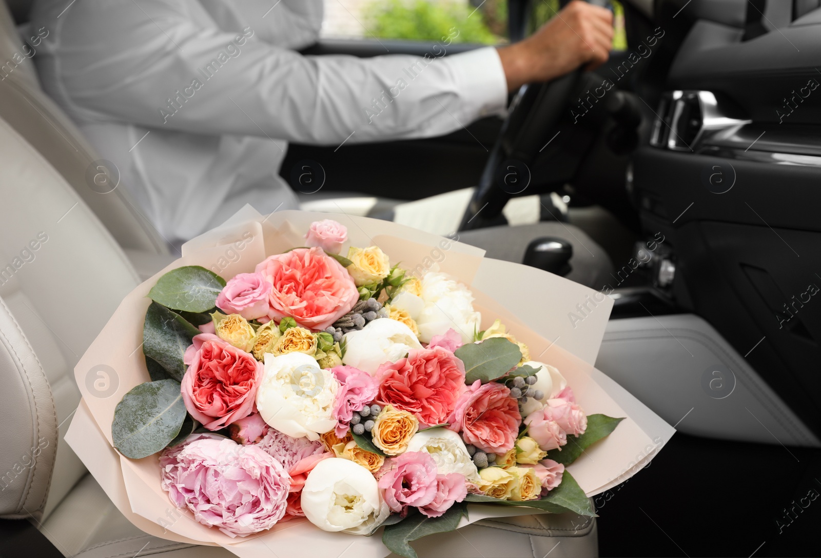 Photo of Young man with beautiful flower bouquet in car, closeup view