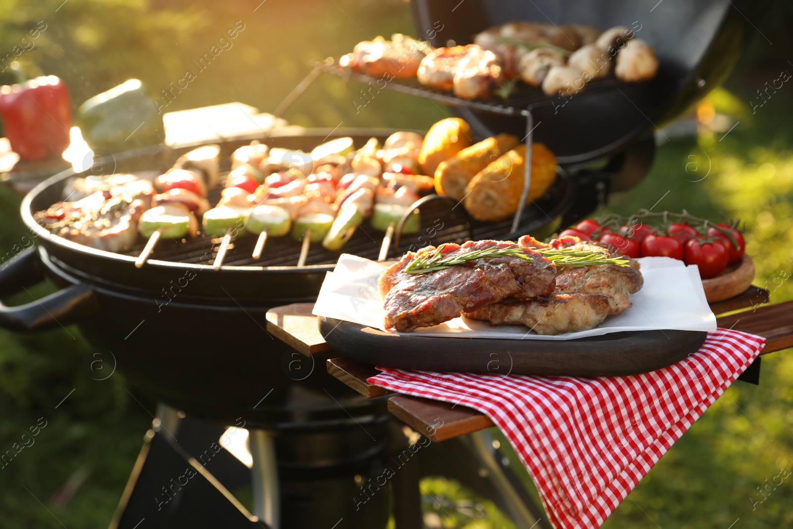 Photo of Tasty cooked meat and cherry tomatoes on table near barbecue grill outdoors