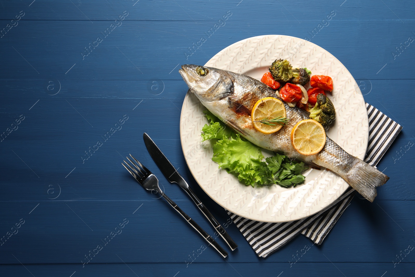 Photo of Delicious baked fish and vegetables served on blue wooden table, top view. Space for text