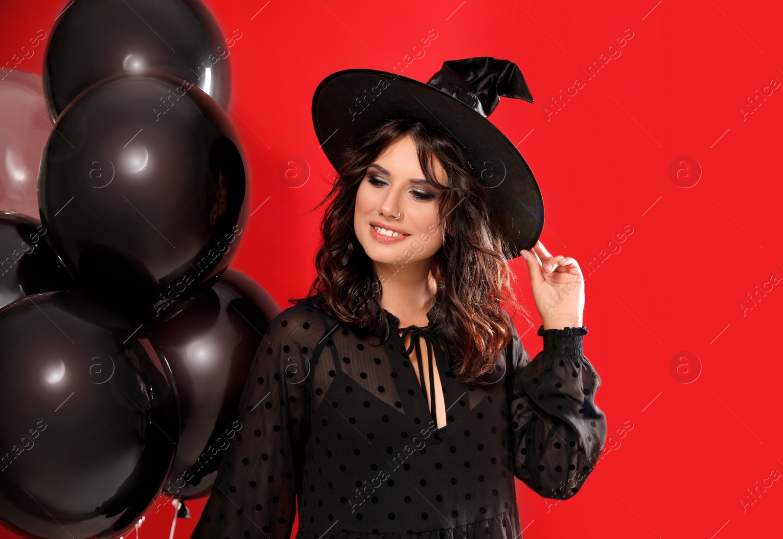 Photo of Beautiful woman in witch costume with balloons on red background. Halloween party