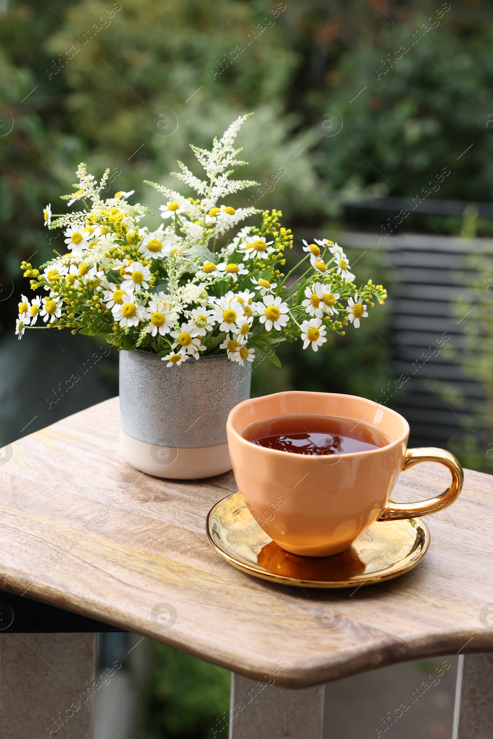 Photo of Cup of delicious chamomile tea and fresh flowers outdoors