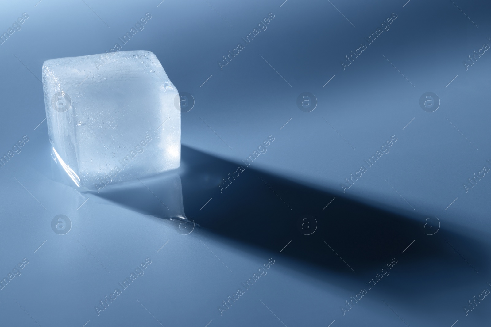 Photo of Crystal clear ice cube on light blue background, space for text