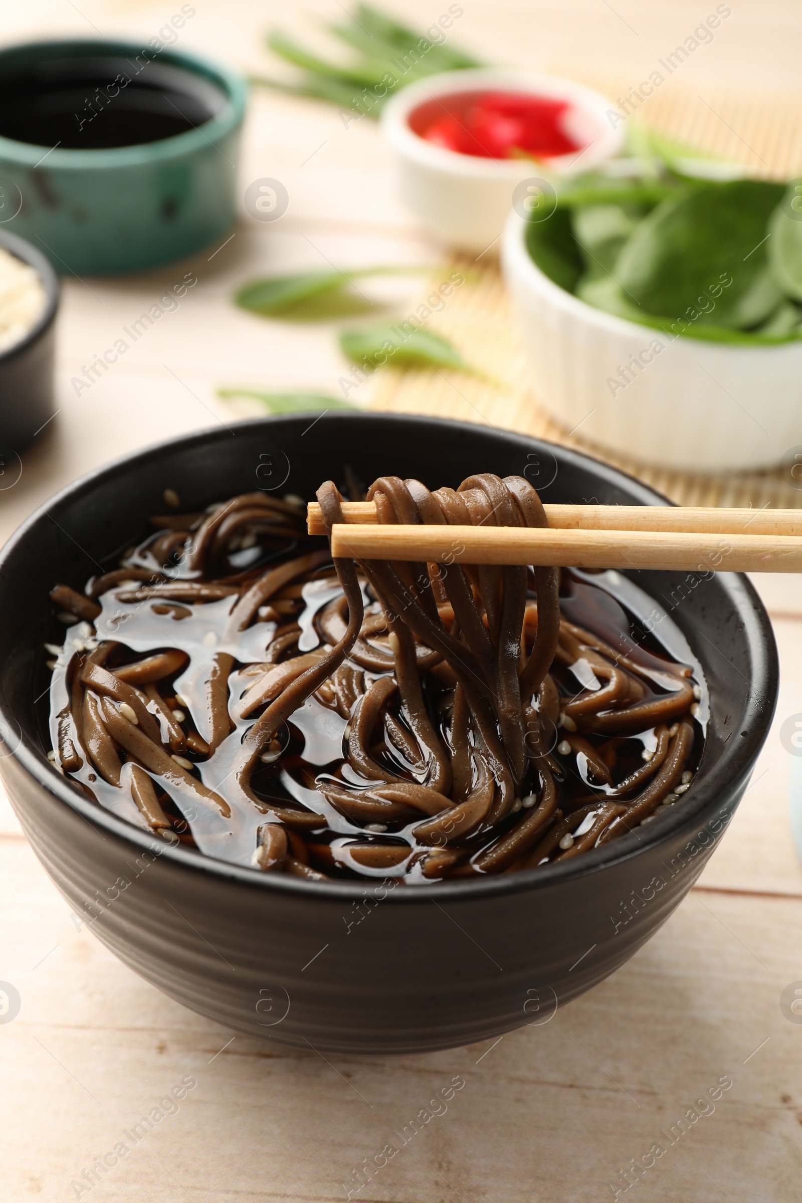 Photo of Eating delicious buckwheat noodle (soba) soup with chopsticks at white wooden table, closeup