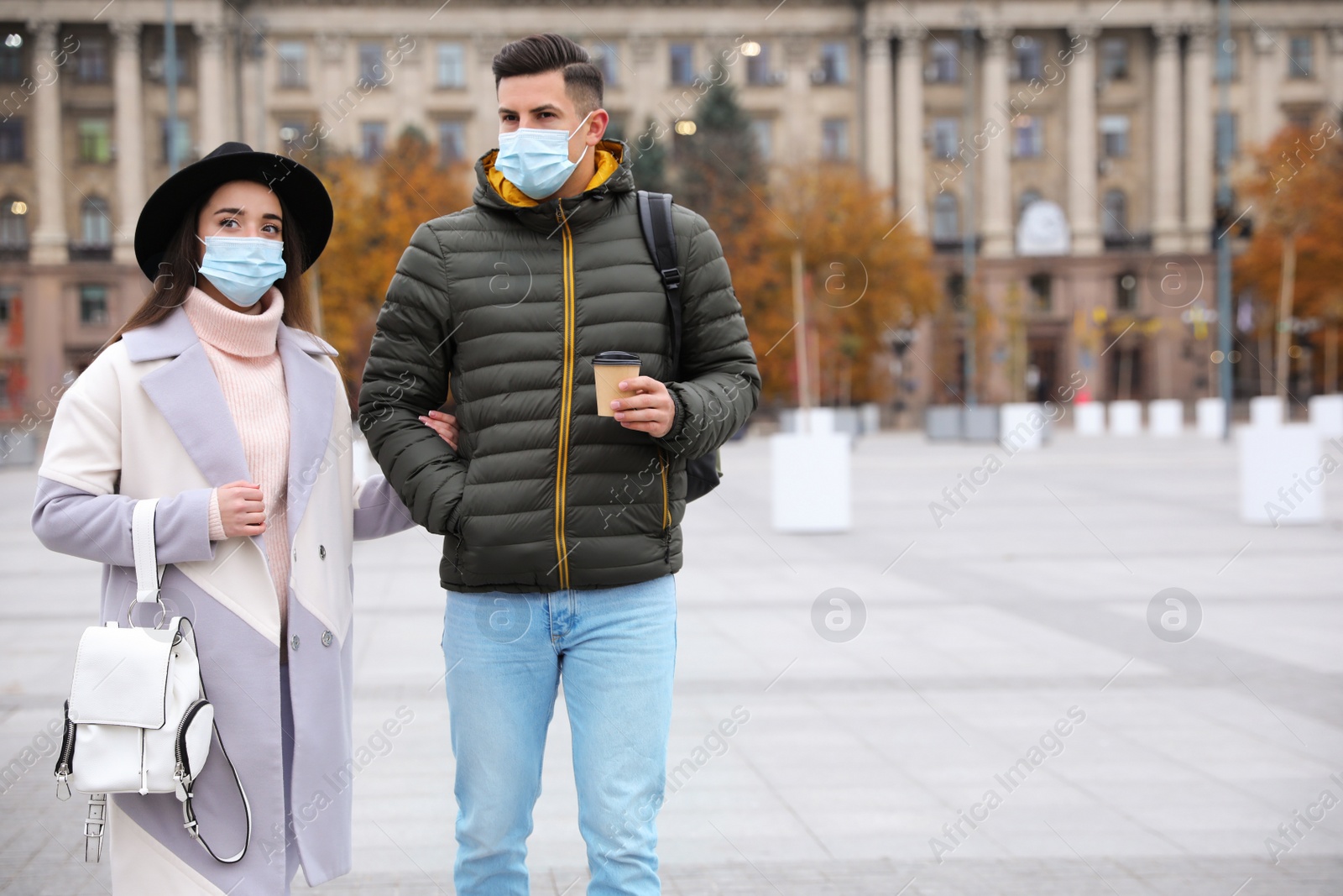 Photo of Couple in medical face masks walking outdoors. Personal protection during COVID-19 pandemic