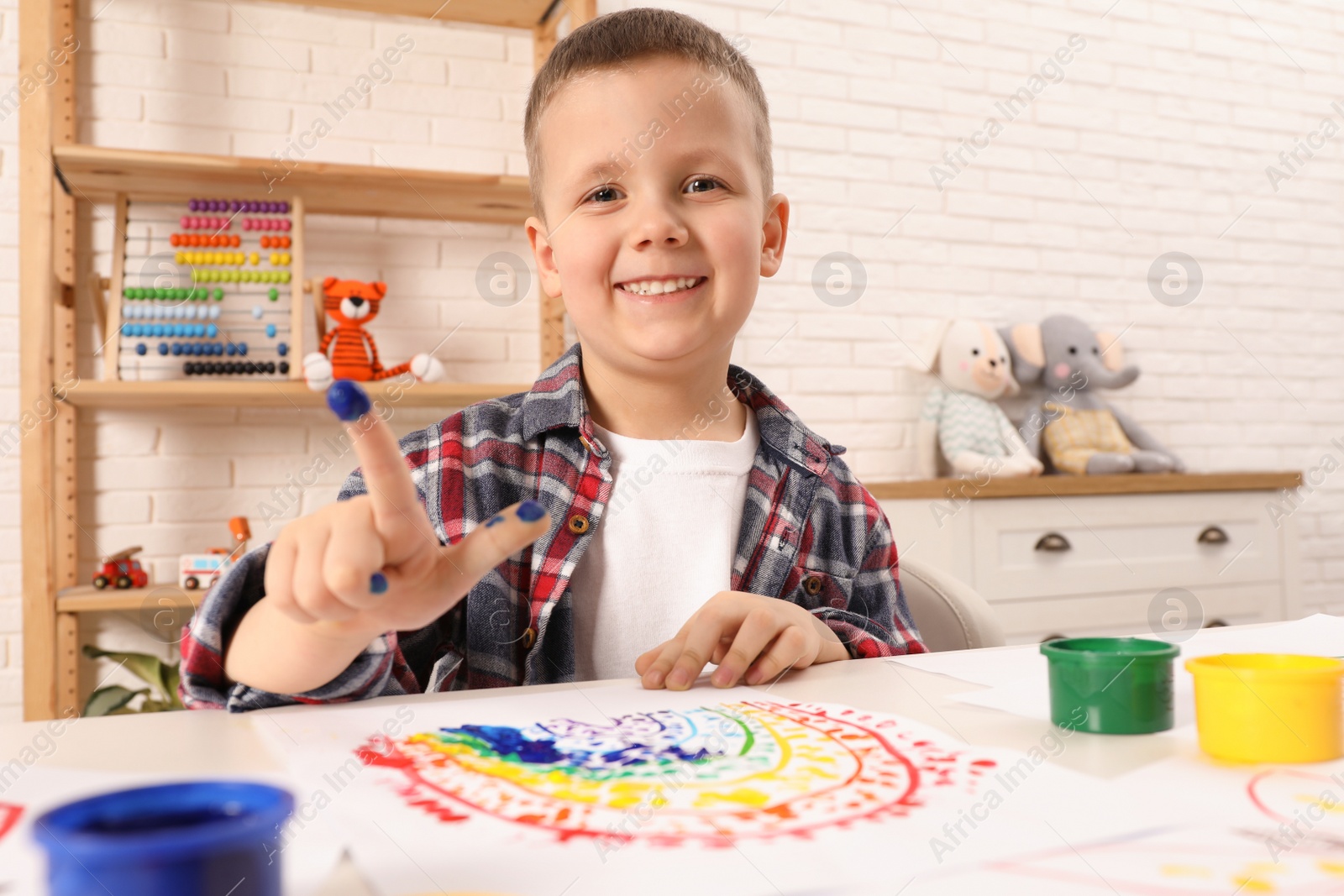 Photo of Little boy painting with finger at white table indoors