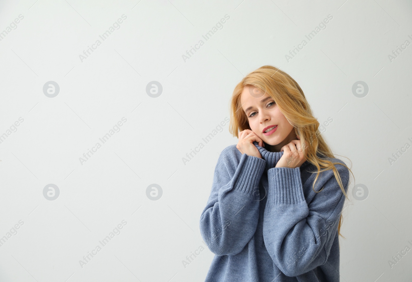 Photo of Beautiful young woman wearing warm blue sweater on light background. Space for text