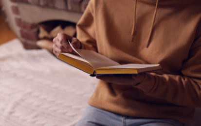 Man reading book near fireplace at home, closeup