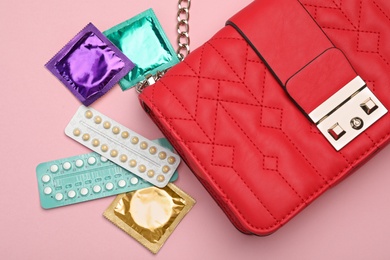 Photo of Purse with condoms and birth control pills on pink background, top view. Safe sex