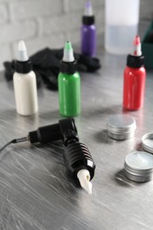 Photo of Modern professional tattoo machine, colorful inks and ointment on table in salon