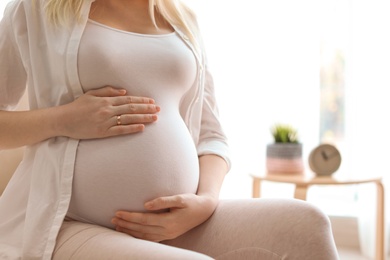 Photo of Pregnant woman sitting in light room at home, closeup