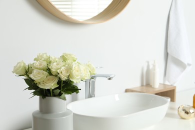 Photo of Vase with beautiful white roses near sink in bathroom
