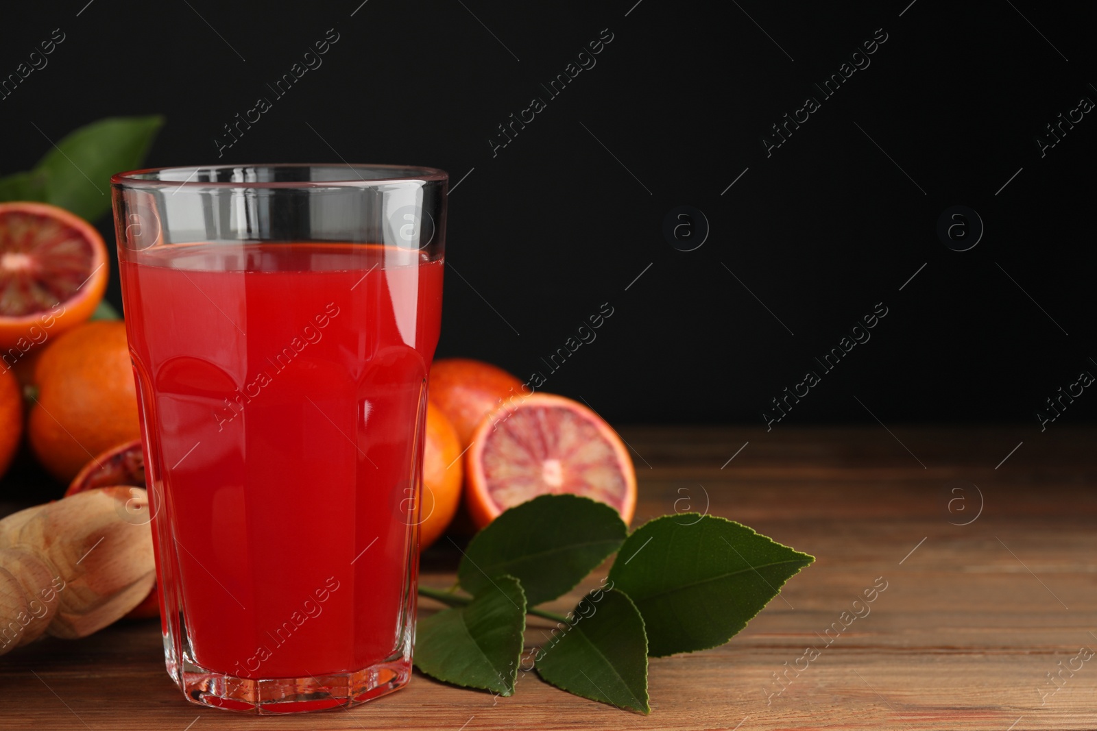 Photo of Tasty sicilian orange juice in glass, fruits and squeezer on wooden table, space for text