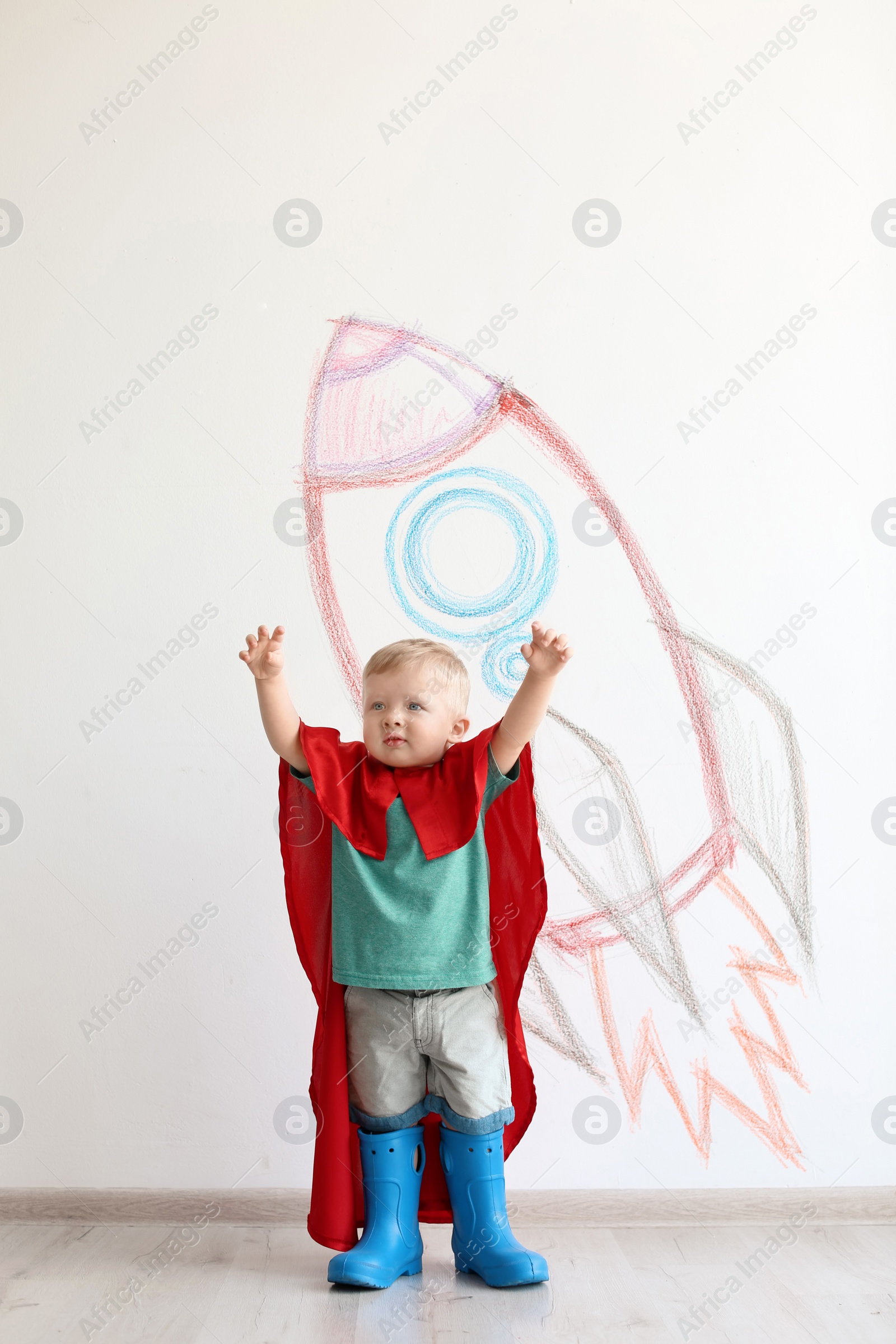 Photo of Adorable little child playing astronaut near wall with drawing of spaceship indoors