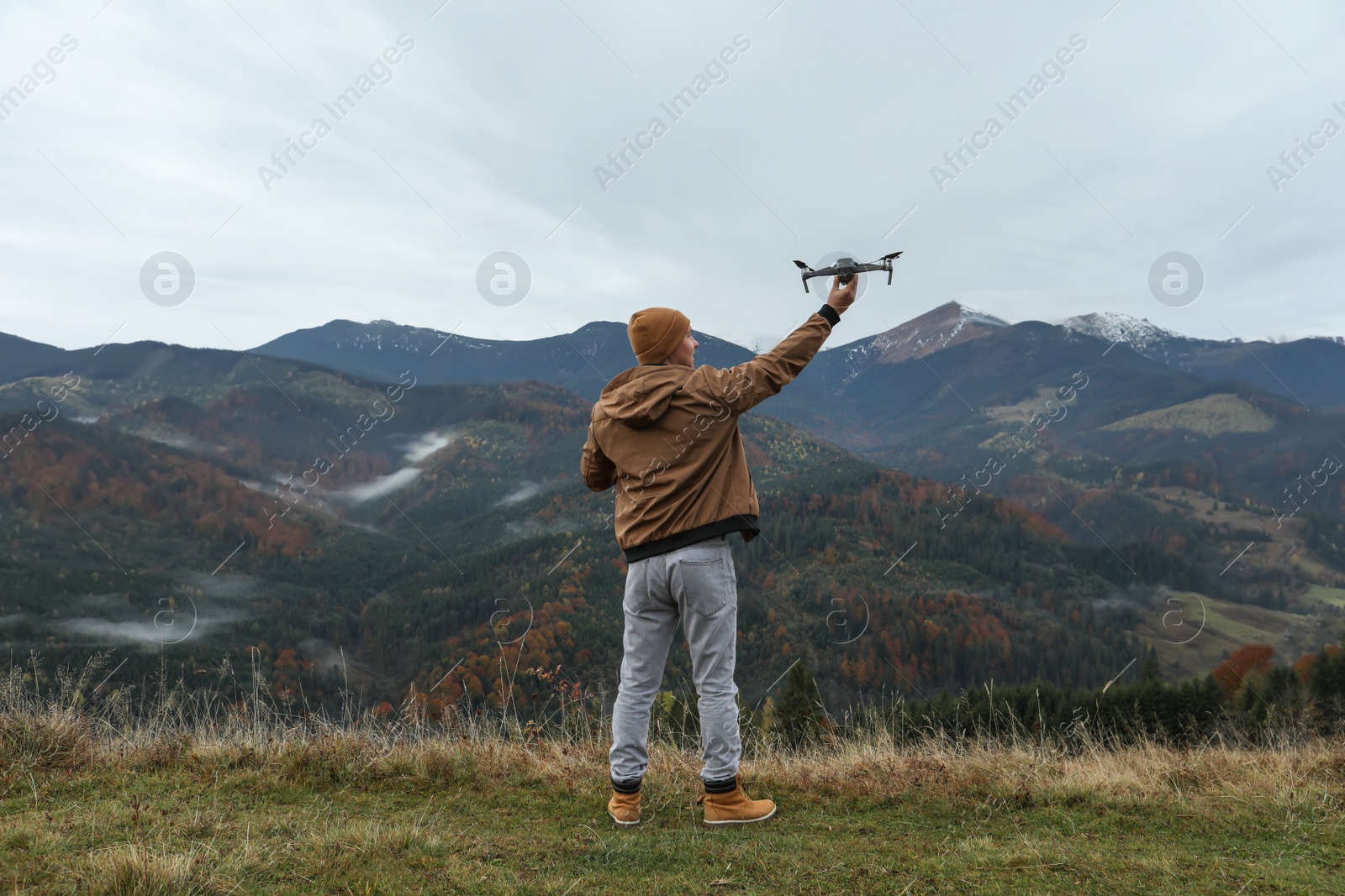 Photo of Young man with modern drone in mountains, back view