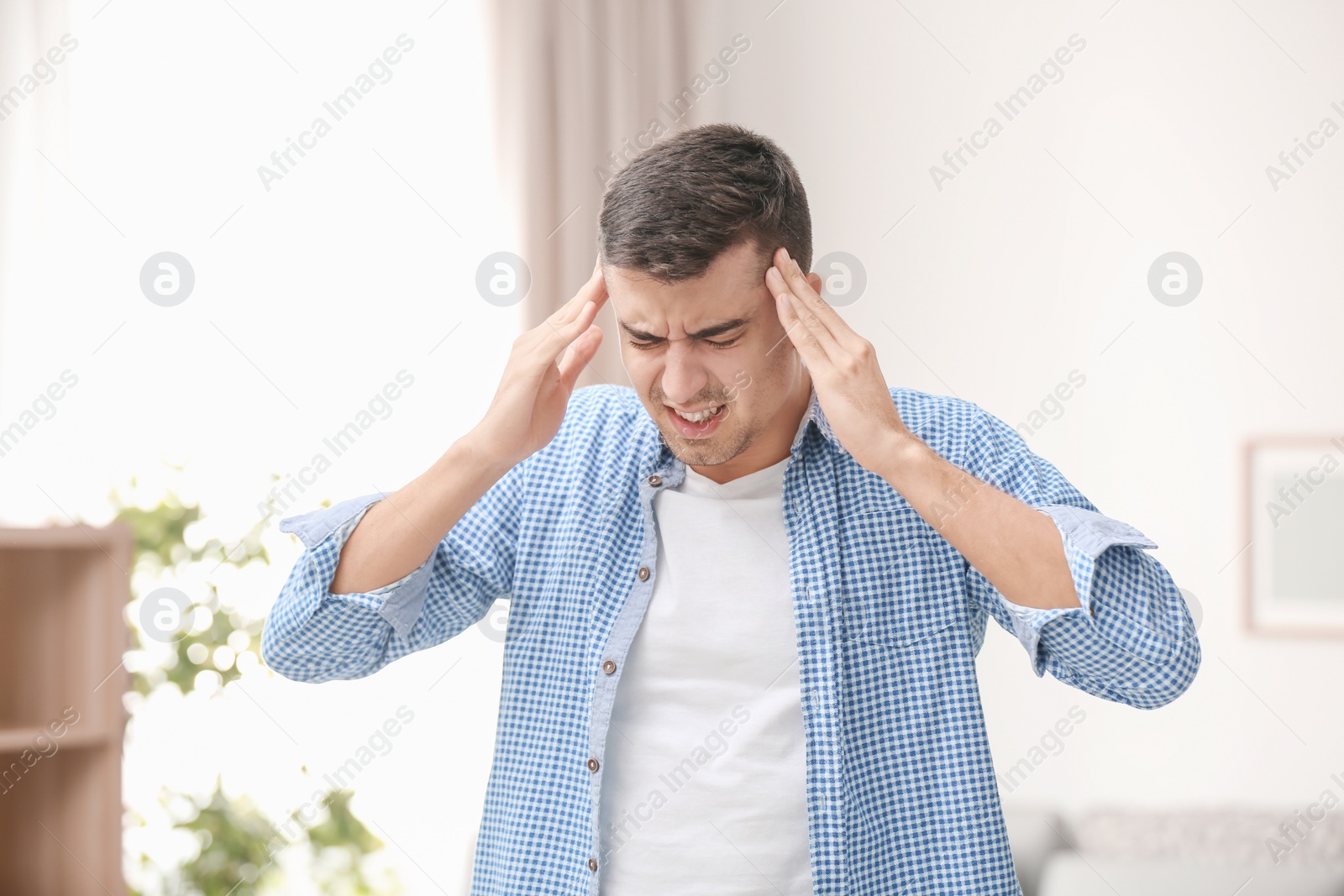 Photo of Young man suffering from headache at home