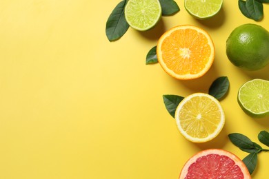 Photo of Different cut and whole citrus fruits on yellow table, flat lay. Space for text