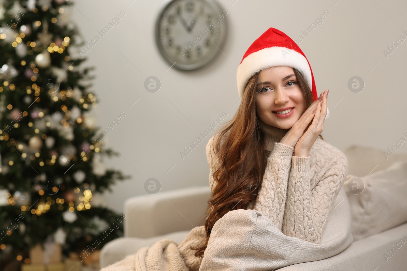 Photo of Beautiful young smiling woman in Santa hat near Christmas tree at home, space for text