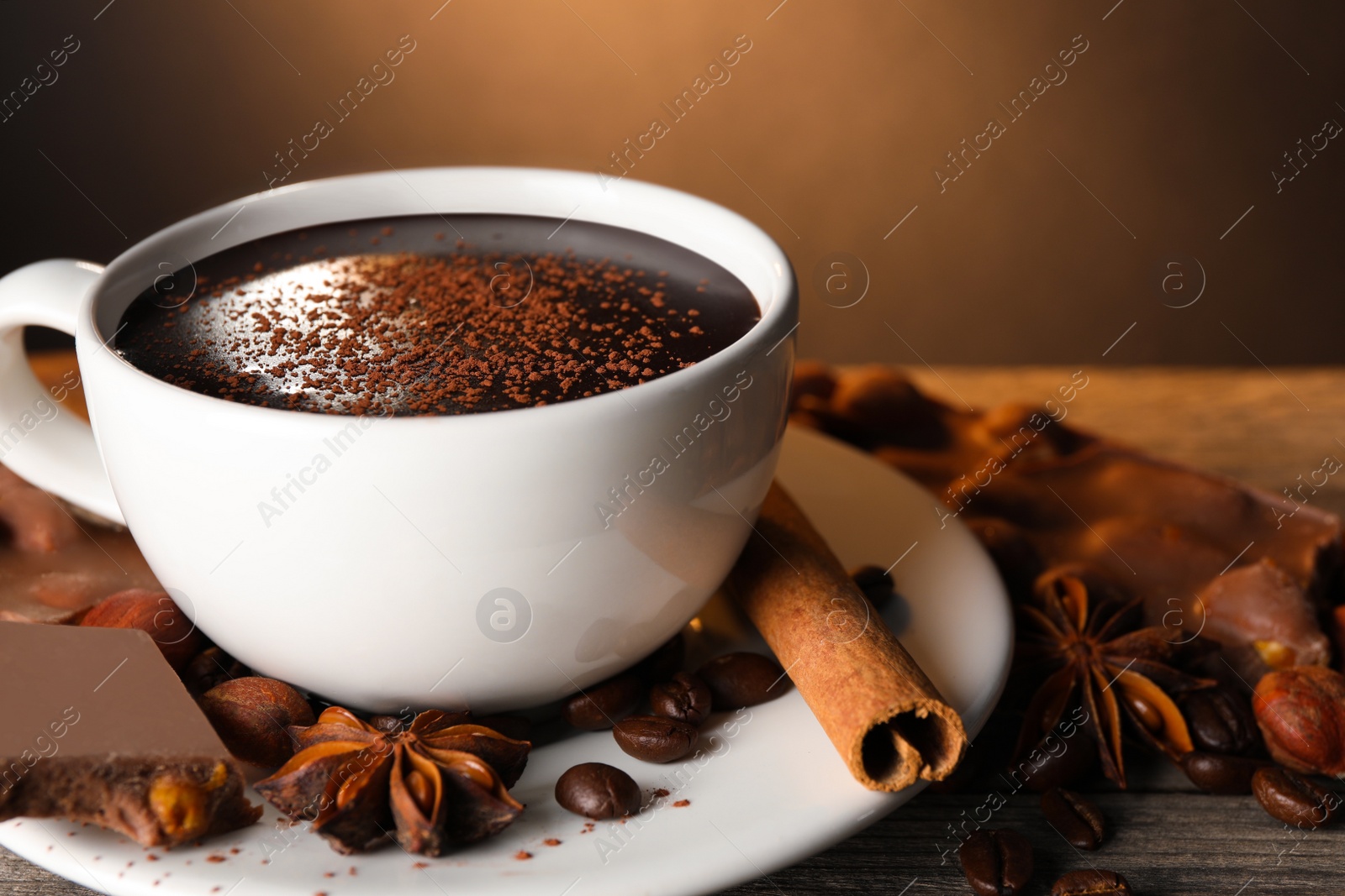 Photo of Cup of delicious hot chocolate, spices and coffee beans on wooden table