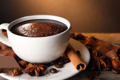 Cup of delicious hot chocolate, spices and coffee beans on wooden table