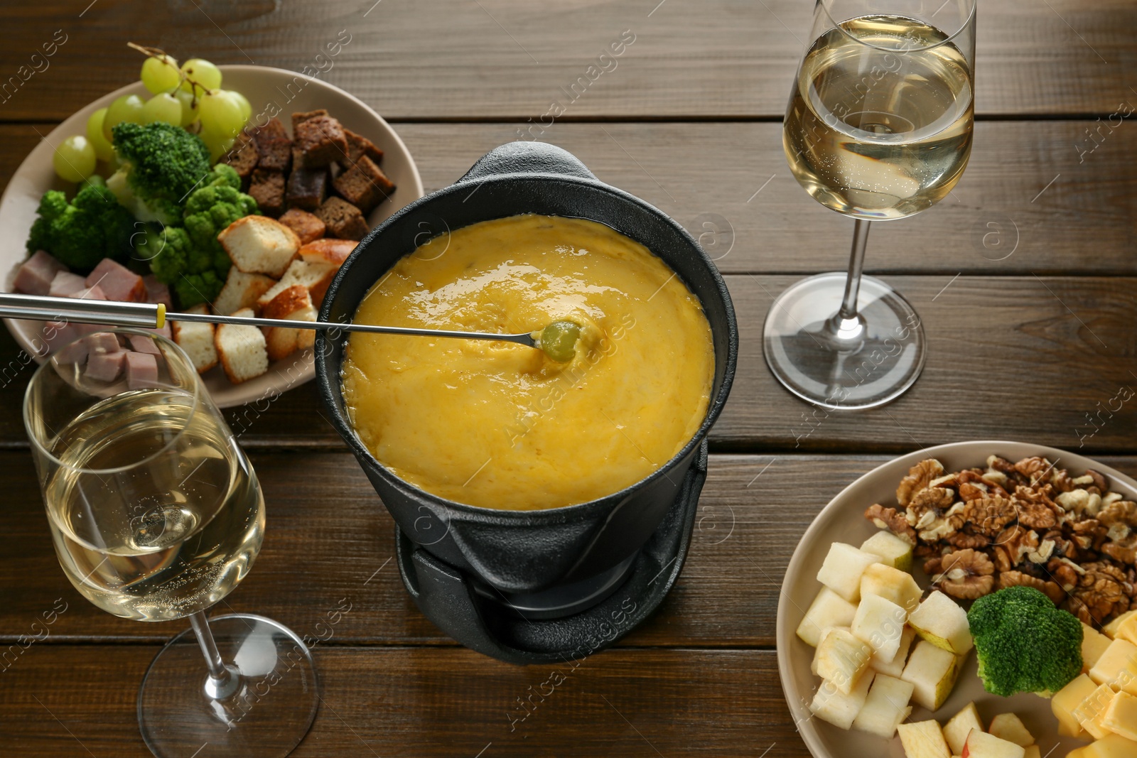 Photo of Fondue pot with melted cheese, glasses of wine and different products on wooden table, above view