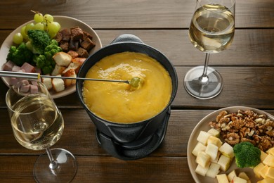 Fondue pot with melted cheese, glasses of wine and different products on wooden table, above view