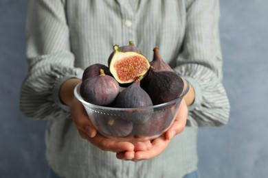 Photo of Woman holding glass bowl with tasty raw figs on light blue background, closeup