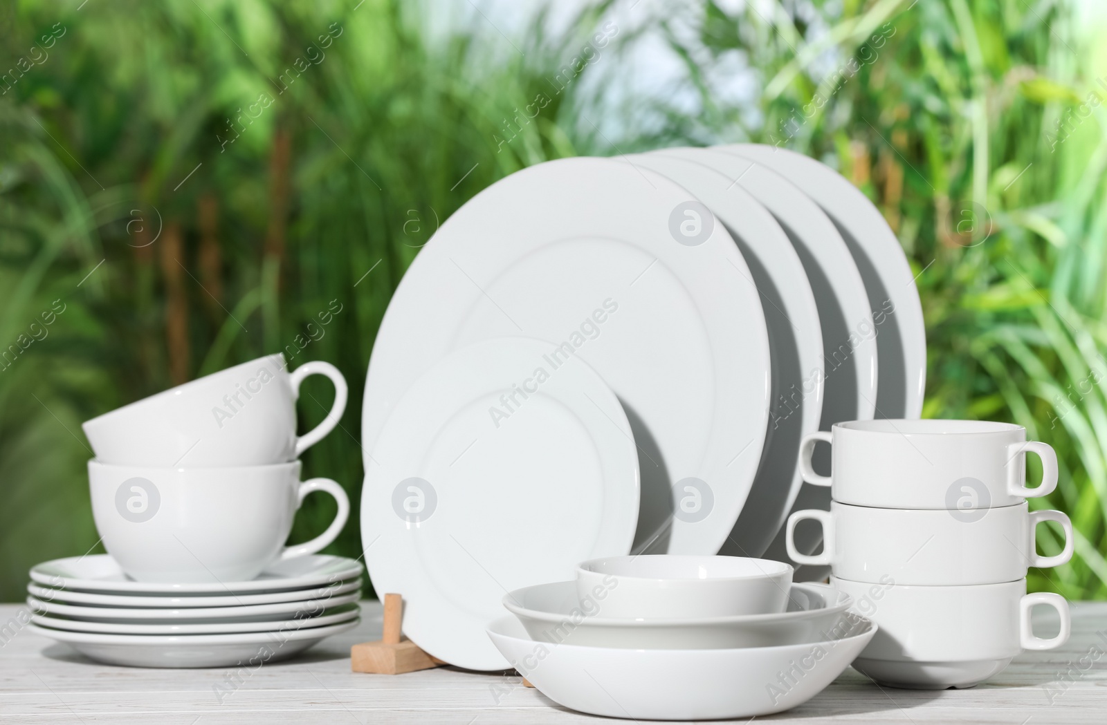 Photo of Set of clean dishware on white table against blurred background