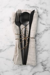 Set of stylish cutlery and napkin on white marble table, top view