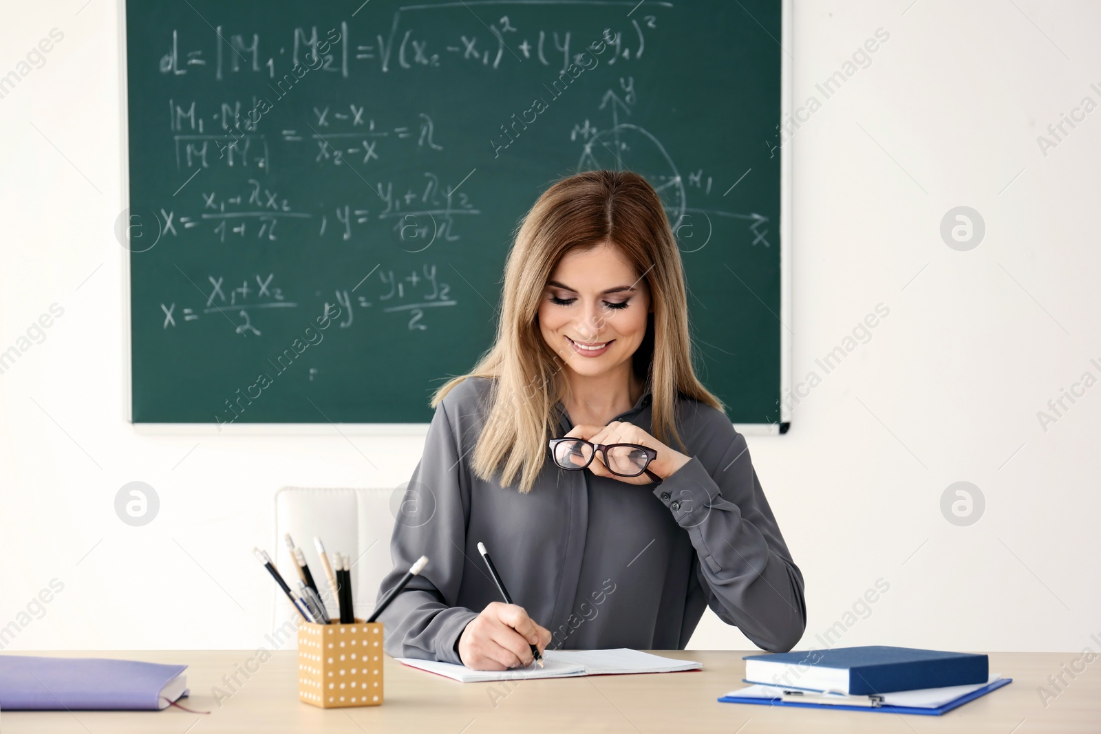 Photo of Young female teacher working at table in classroom