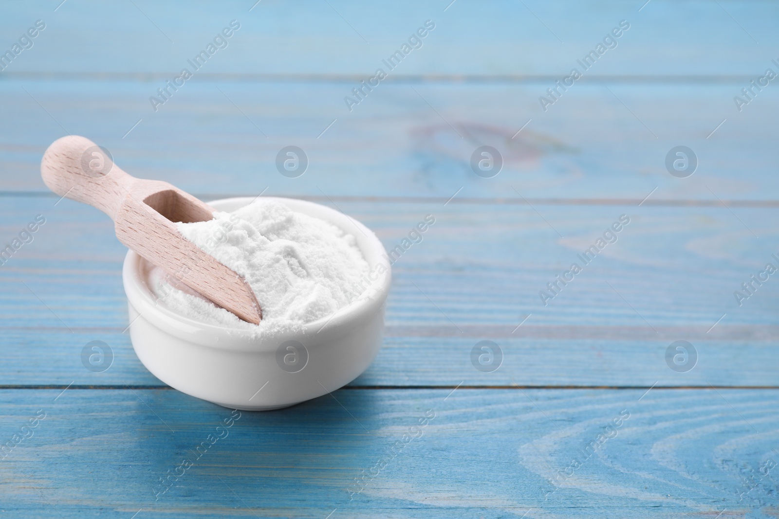 Photo of Bowl of fructose powder on light blue wooden table. Space for text