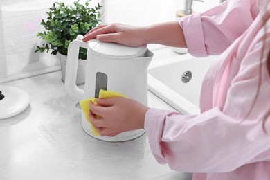 Woman cleaning electric kettle with sponge at countertop in kitchen, closeup