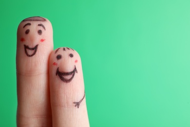 Photo of Two fingers with drawings of happy faces on green background, space for text. Spending time together