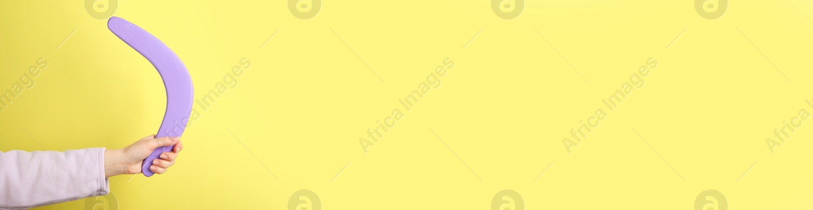 Photo of Woman holding boomerang on yellow background, closeup