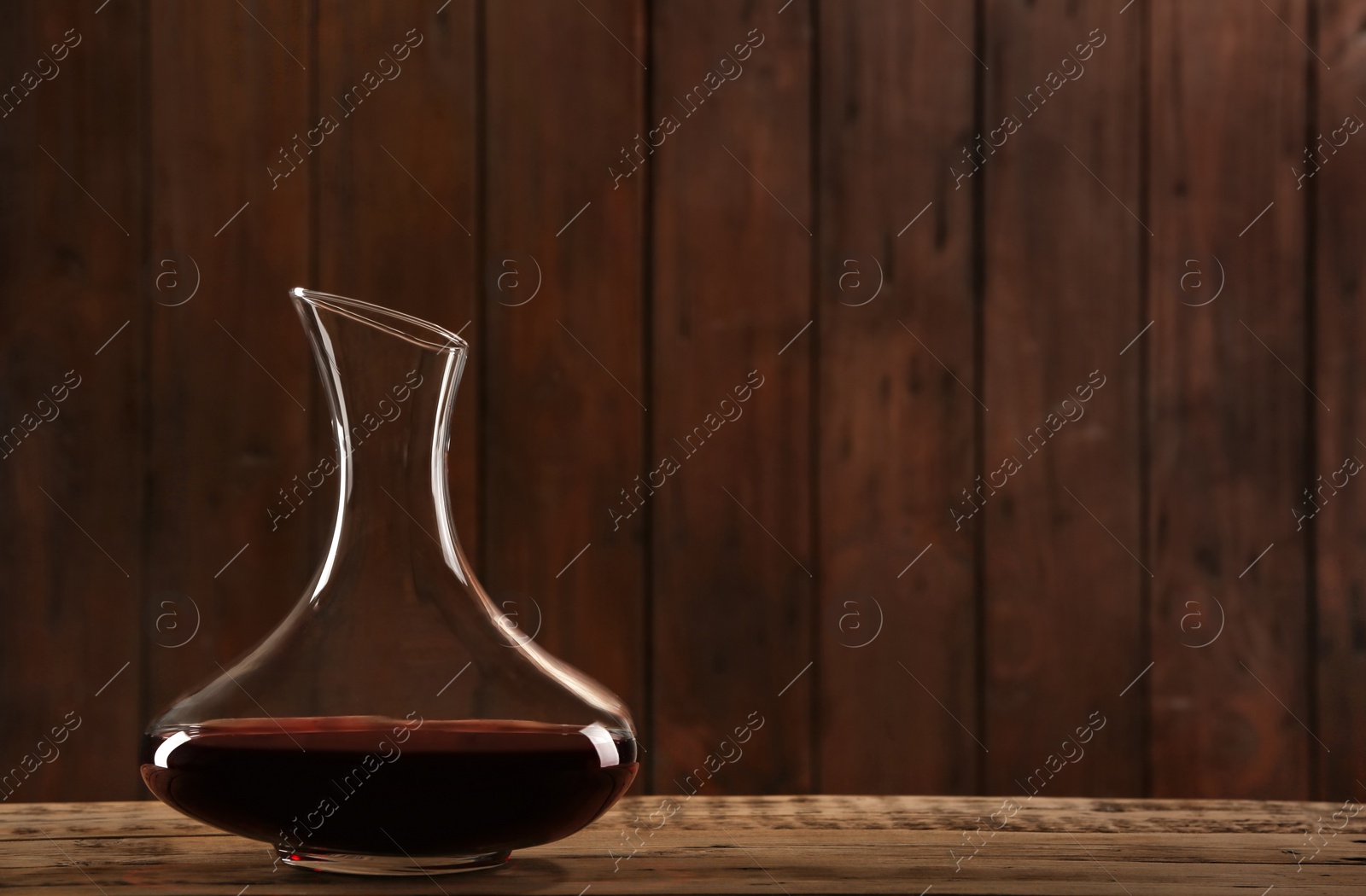 Photo of Elegant decanter with red wine on table against dark background