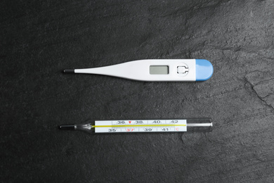 Photo of Mercury and digital thermometers on black slate background, flat lay