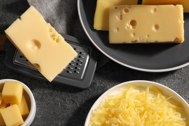 Grated, whole pieces of cheese and grater on dark textured table, flat lay