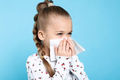 Photo of Sick girl blowing nose in tissue on turquoise background. Cold symptoms