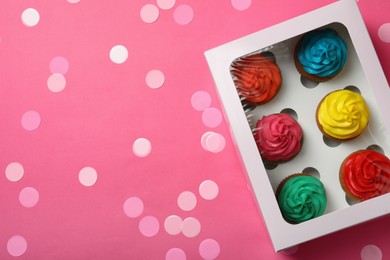 Photo of Box with different cupcakes and confetti on pink background, flat lay. Space for text