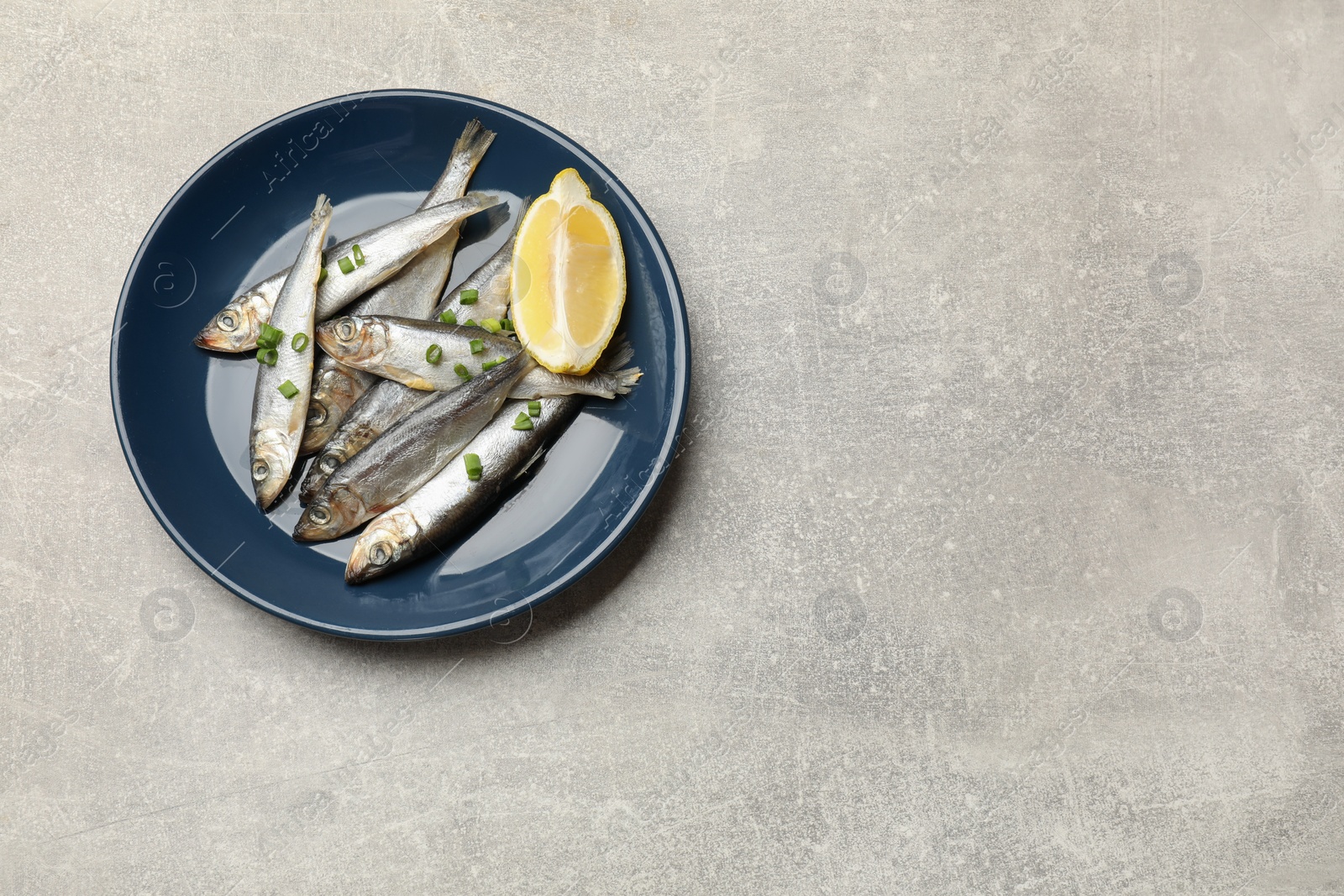 Photo of Fresh raw sprats, green onion and cut lemon on grey table, top view. Space for text