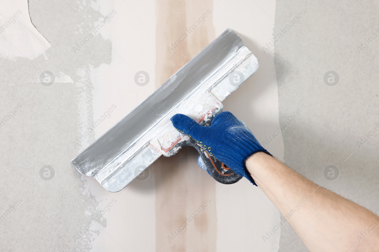 Photo of Worker plastering wall with putty knife indoors, closeup